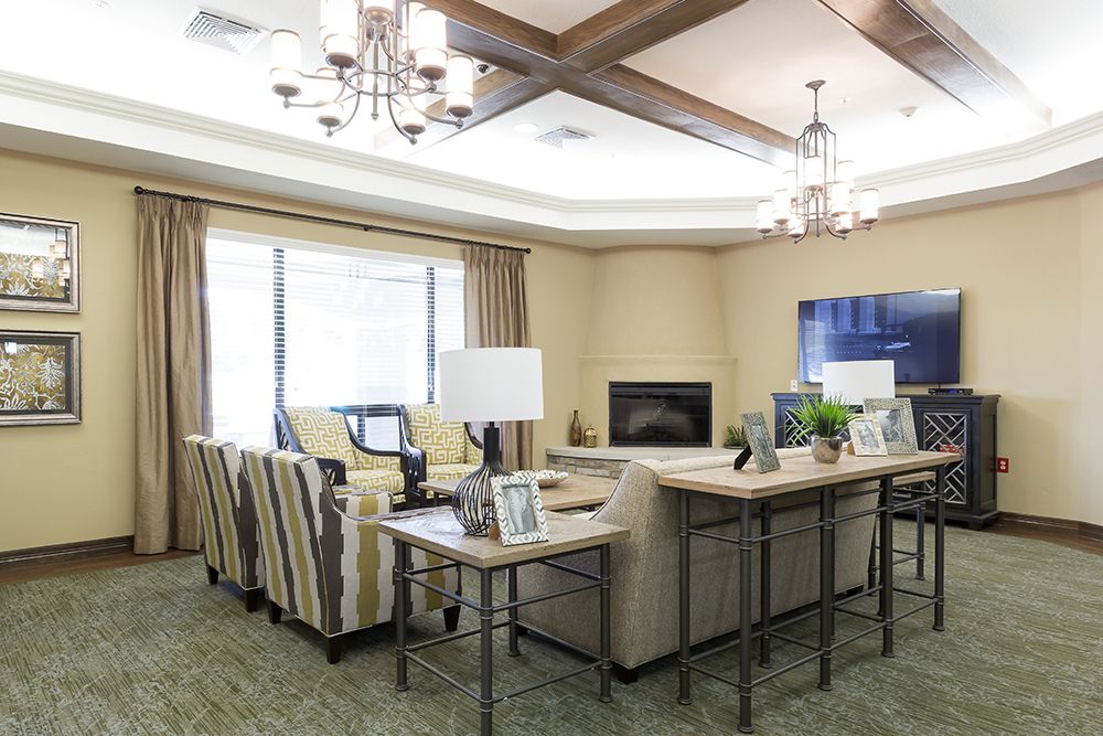 A cozy living room with elegant furniture, a fireplace, and a television, illuminated by chandeliers.