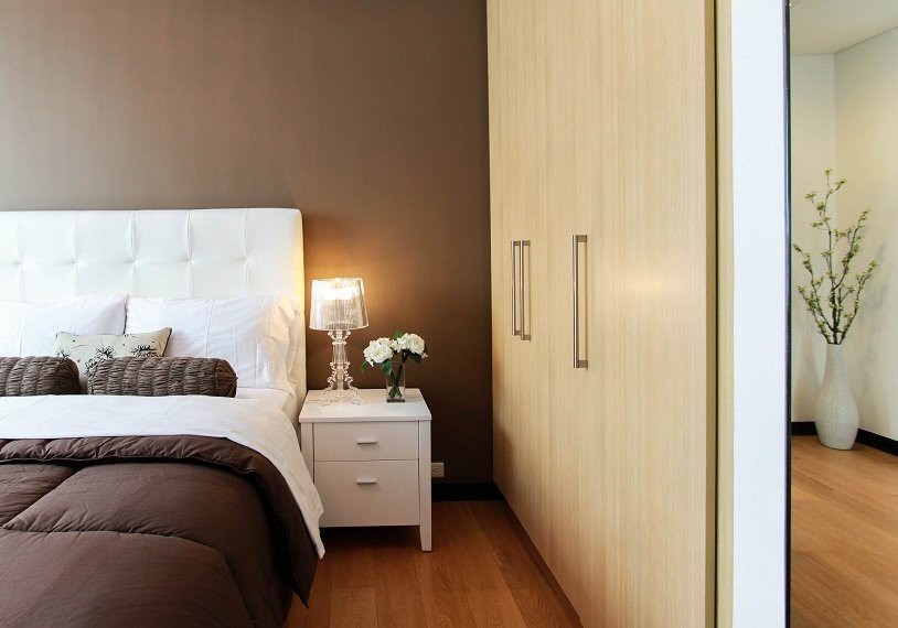 A cozy bedroom with a warm color scheme featuring a bed, nightstand with lamp, and built-in wardrobe.