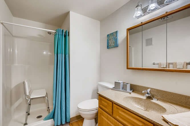 A clean and simple bathroom with a shower, sink, toilet, and blue shower curtain.