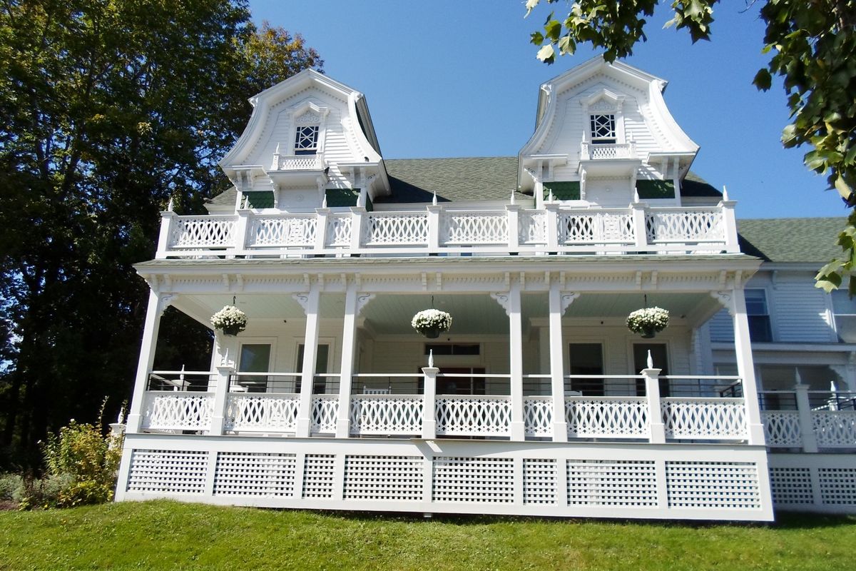 A charming white Victorian house with a spacious porch and hanging plants.