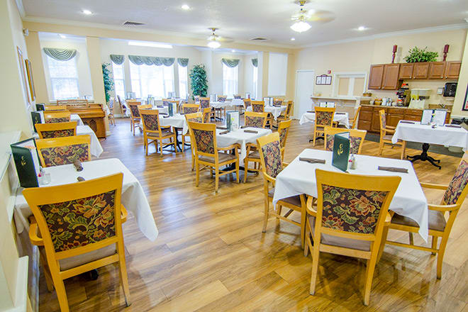 A bright dining room with neatly arranged tables and chairs, featuring wood flooring and large windows.