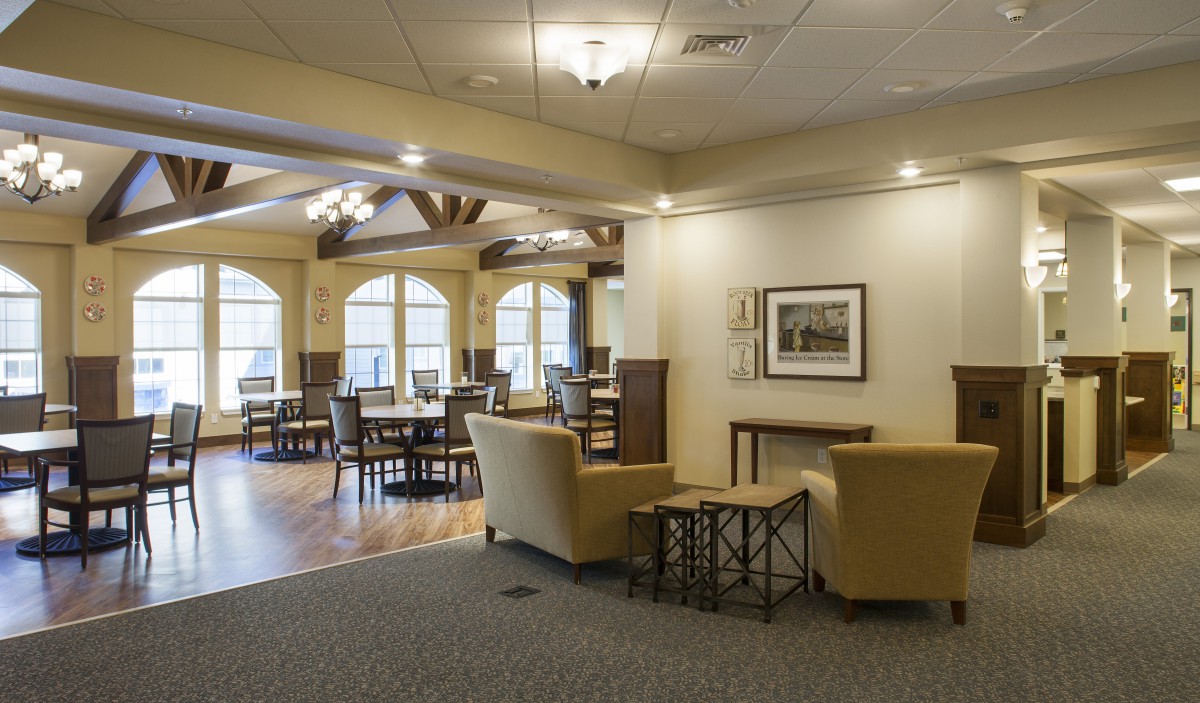 A cozy interior lounge area featuring comfortable seating and dining tables, illuminated by natural light through large windows.