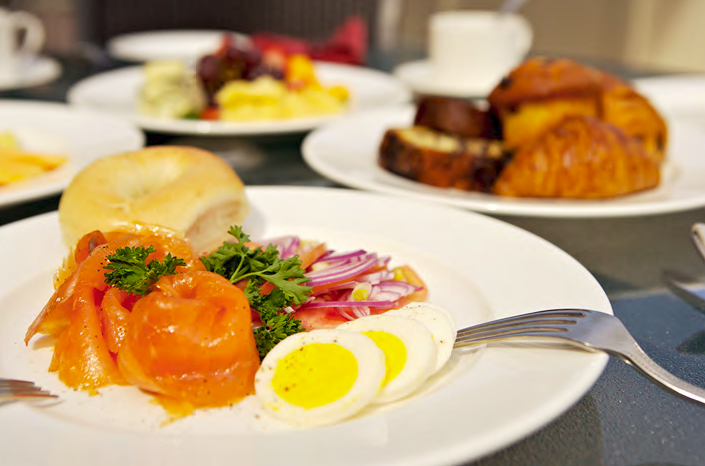 A delicious breakfast spread featuring smoked salmon, hard-boiled eggs, and a bagel with a side of pastries and coffee.