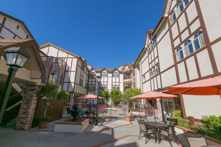A courtyard with outdoor seating and umbrellas set against a backdrop of Tudor-style buildings on a sunny day.