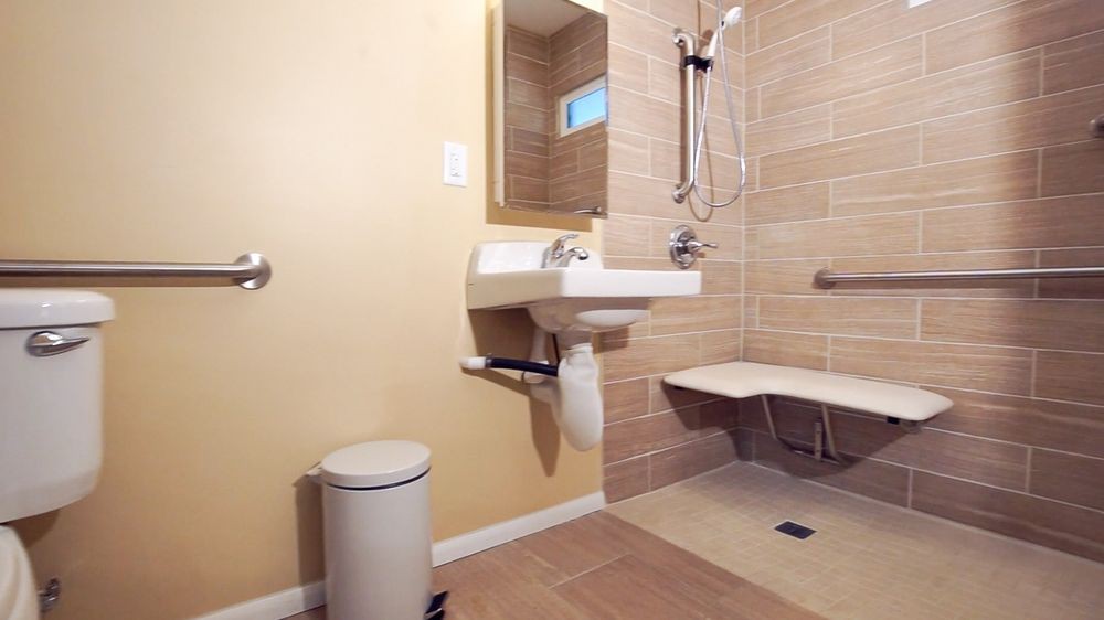 An accessible bathroom with a wall-mounted sink, shower area with a seat, and grab bars for support.