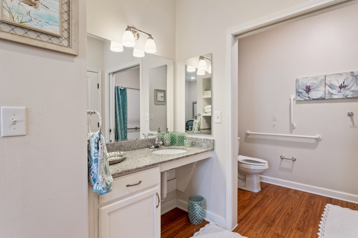 A bathroom featuring a modern vanity with a large mirror, well-lit by overhead lights.