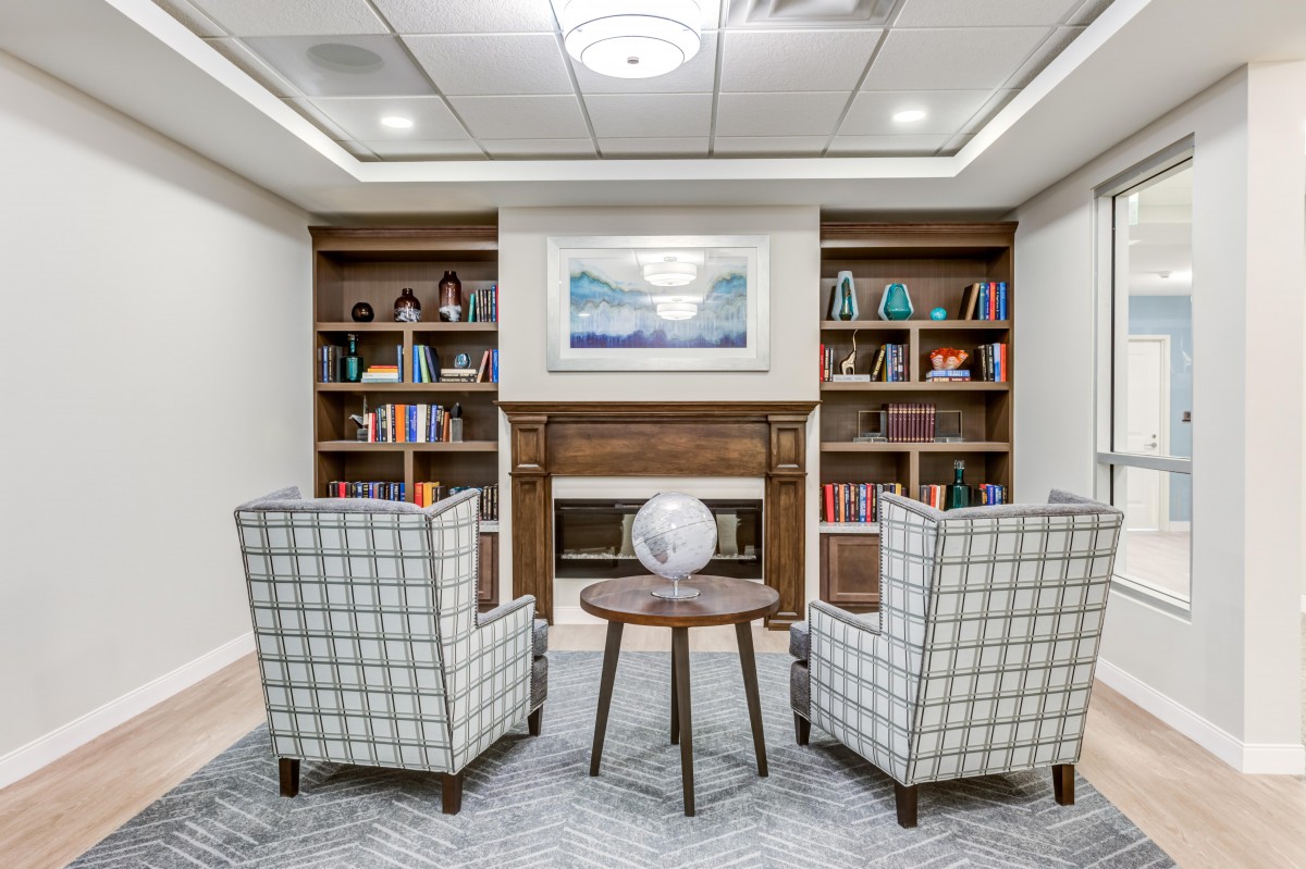 A cozy library with two armchairs facing a fireplace, surrounded by bookshelves and a small coffee table holding a globe.