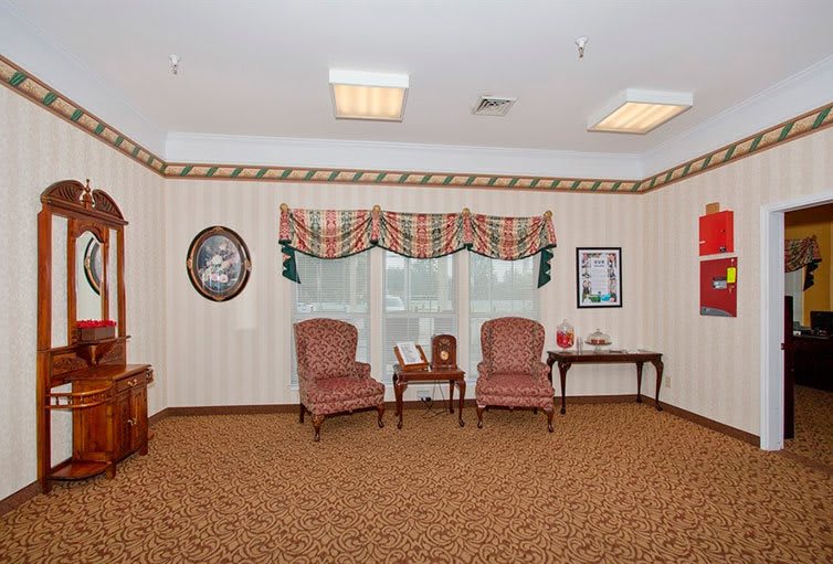 A cozy room with two upholstered chairs, a small table, decorative curtains, and a carpeted floor.
