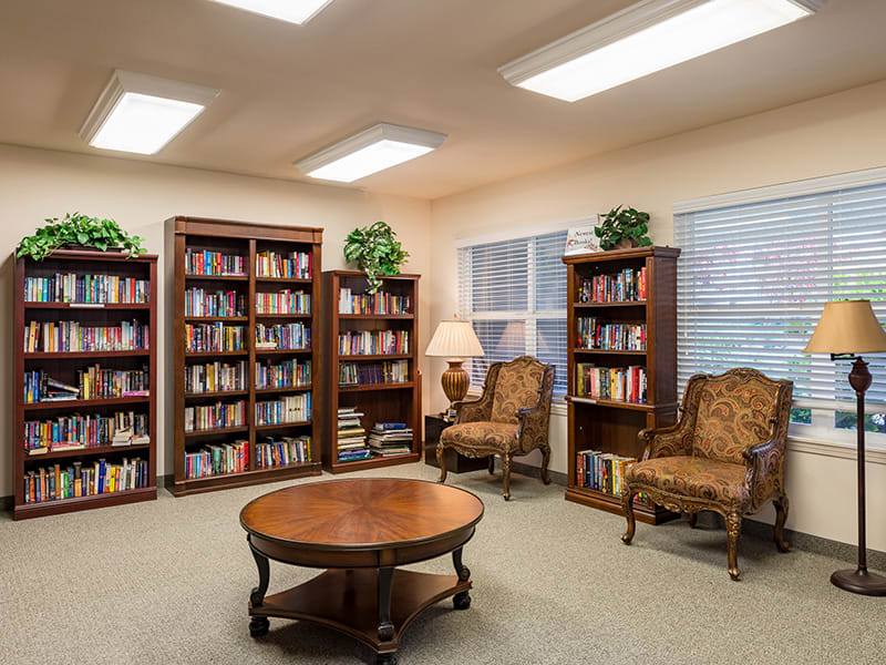A cozy library reading area with bookshelves, chairs, and a table.
