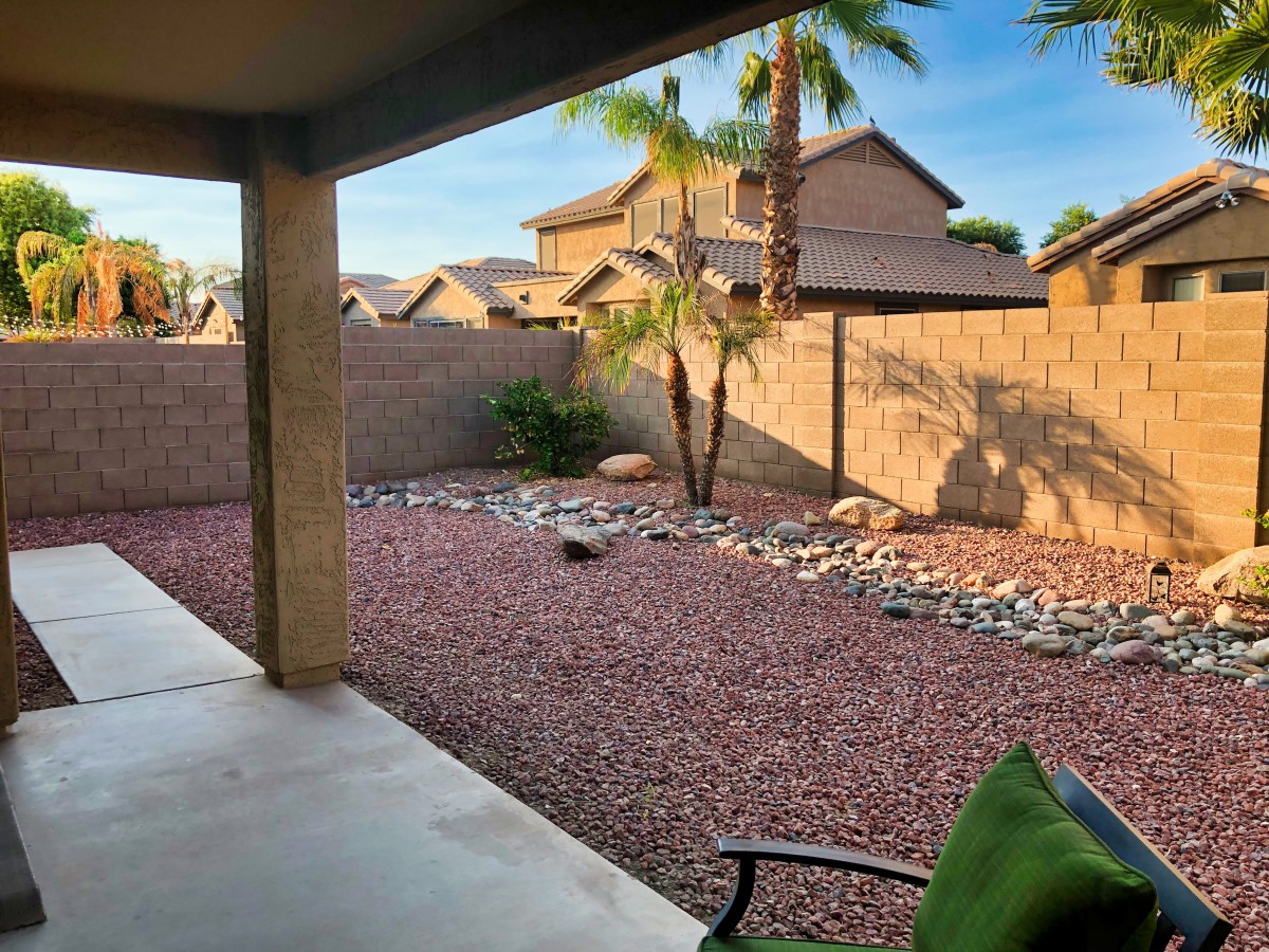 A serene backyard with desert landscaping, featuring a patio area and palm tree.