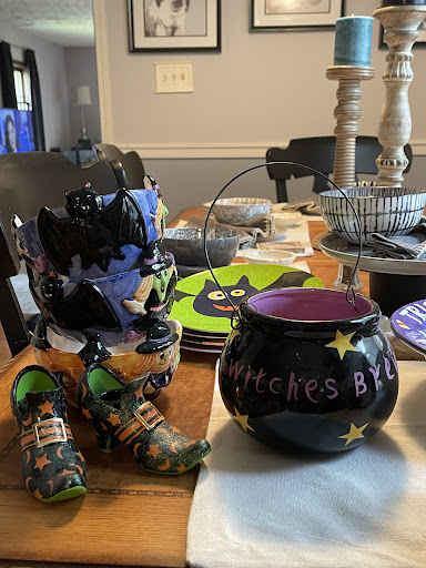 A festive Halloween table setup featuring a black cauldron labeled 'Witches Brew', colorful plates, and fun costume shoes.