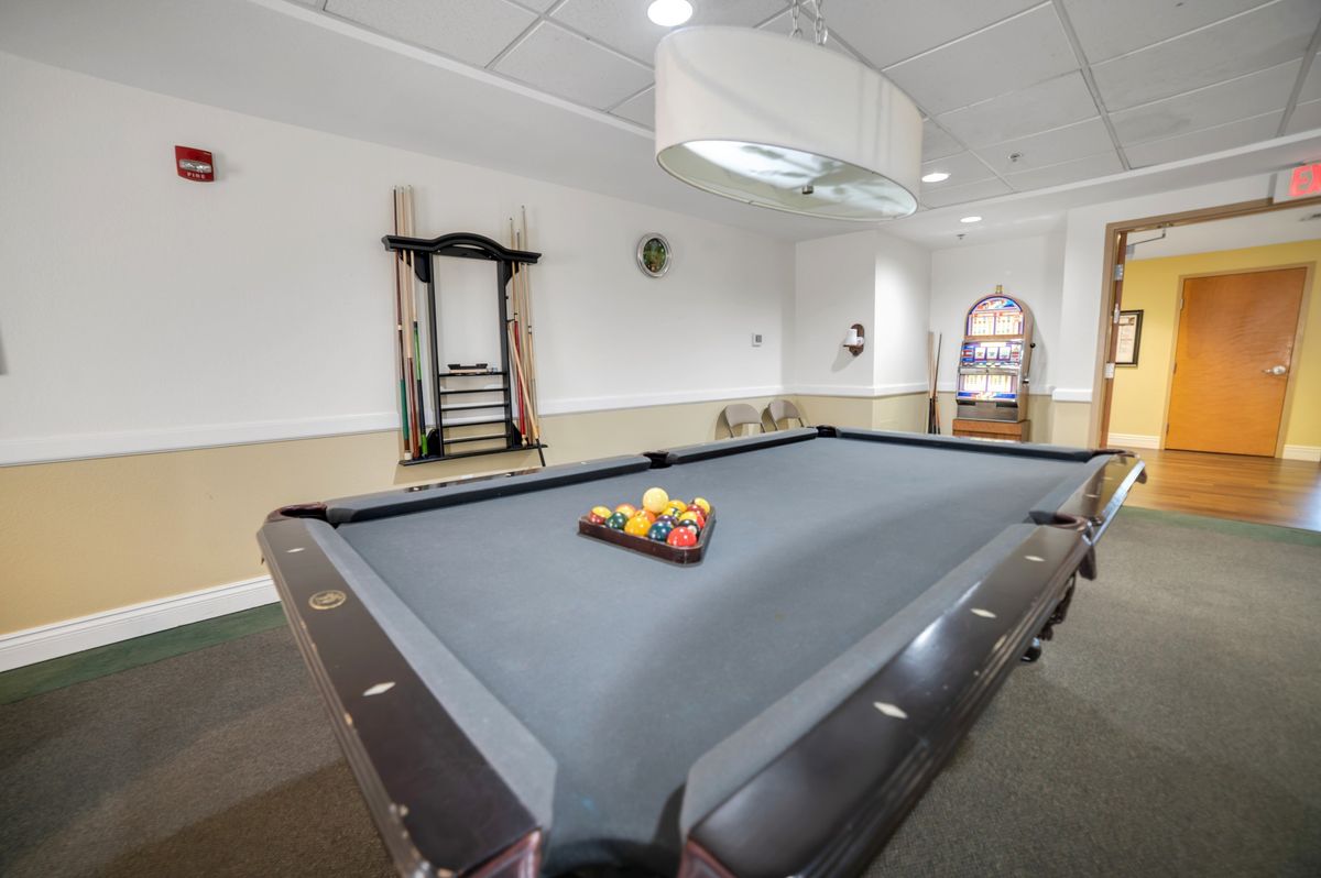 A game room featuring a pool table with billiard balls racked and cue sticks on the wall.