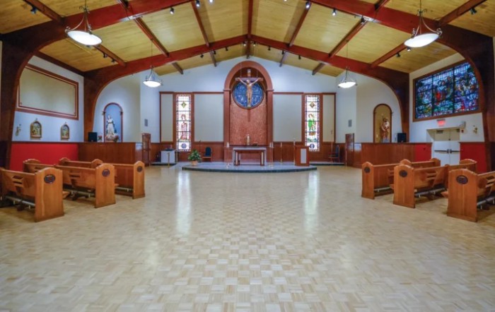 The interior of a church with an altar, rows of pews, and stained glass windows.