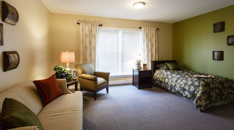 A cozy bedroom with a bed, armchair, and large window with curtains.