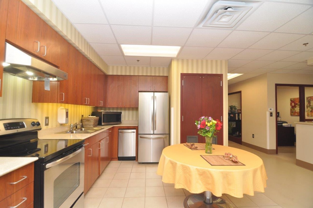 A modern kitchen featuring stainless steel appliances, wood cabinets, and a round table adorned with flowers.