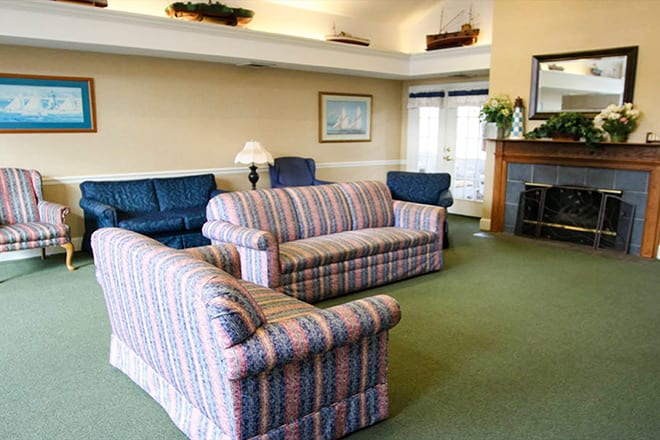 A cozy living room with striped sofas, a fireplace, and a carpeted floor.