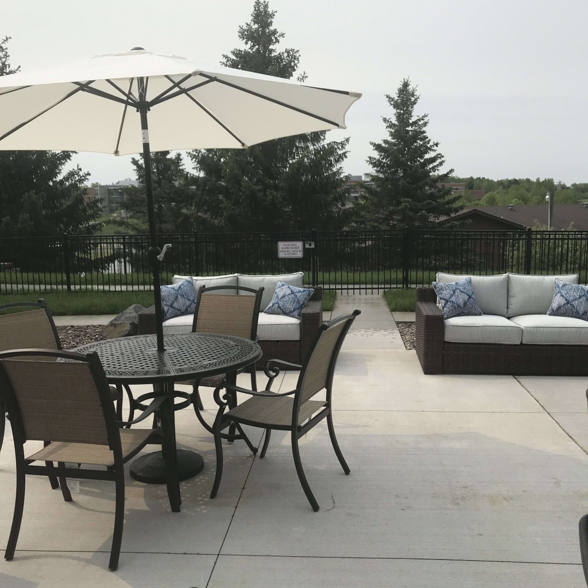A patio featuring outdoor furniture, including a table with chairs and an umbrella, set against a backdrop of trees.