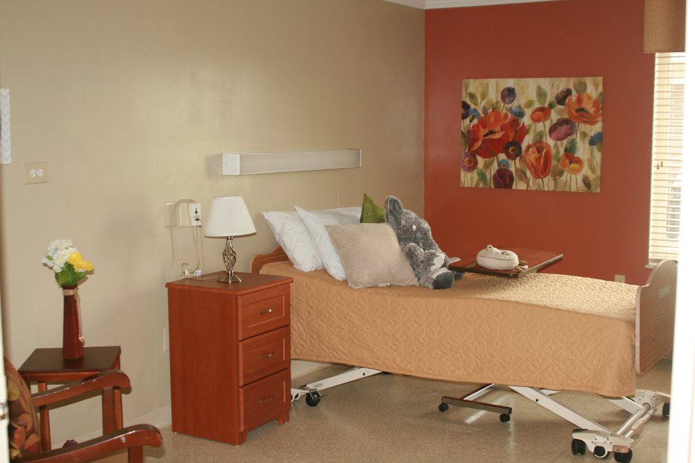 A well-decorated hospital room featuring a bed, nightstand with a lamp, and floral artwork on the wall.