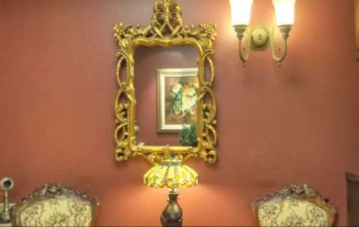 Elegant interior decor featuring a gilded mirror, a decorative lamp, and framed artwork.