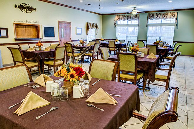 A neatly arranged dining room with tables set for a meal, featuring floral centerpieces.