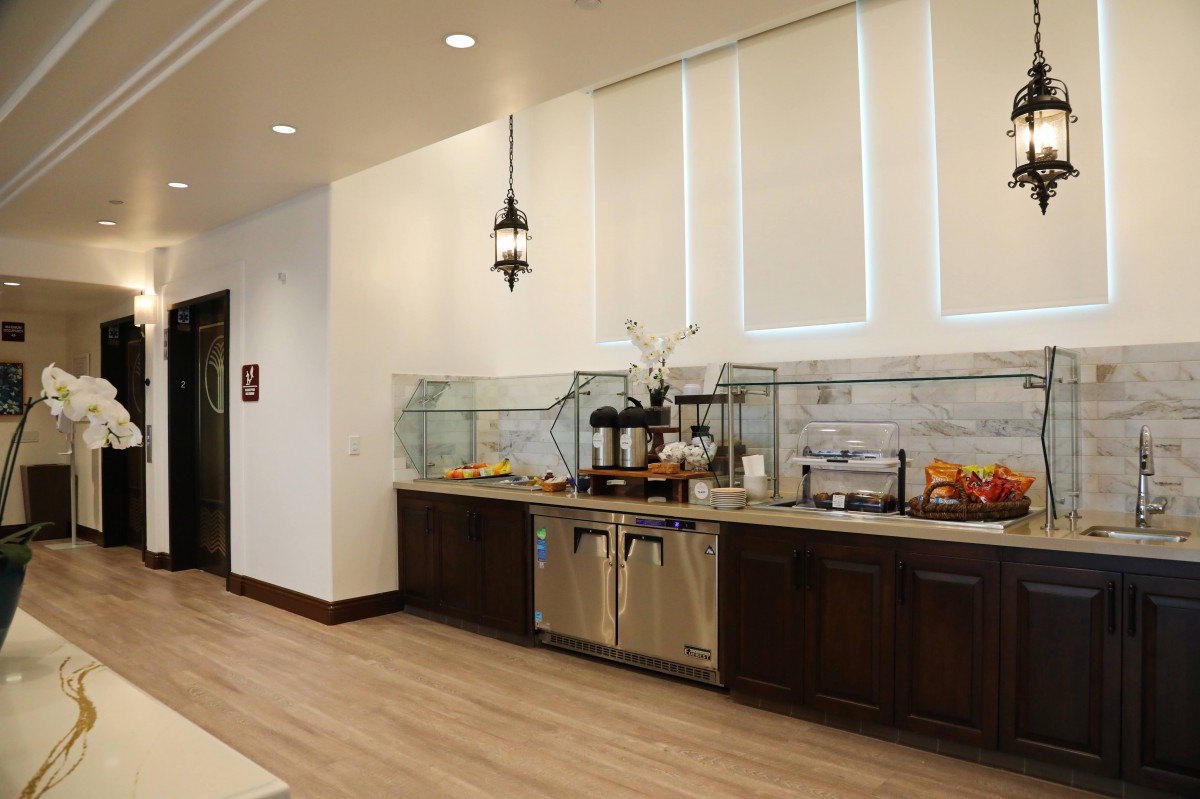 A modern buffet setup with various food and drink options on a countertop, featuring sleek cabinets and bright interior design.