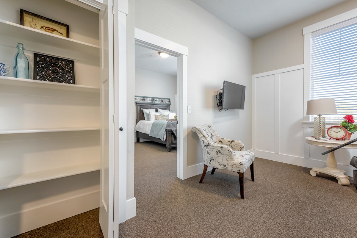 A modern bedroom with a cozy setup featuring a large bed, a mounted television, an elegant chair, and built-in shelves.