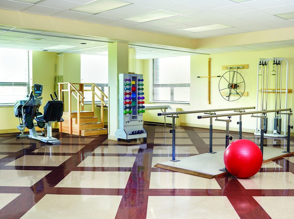 A well-equipped physical therapy room with various rehabilitation tools and exercise equipment, including parallel bars and a large red therapy ball.