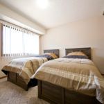 A cozy bedroom featuring two twin beds with neutral-colored bedspreads, illuminated by natural light from a large window.