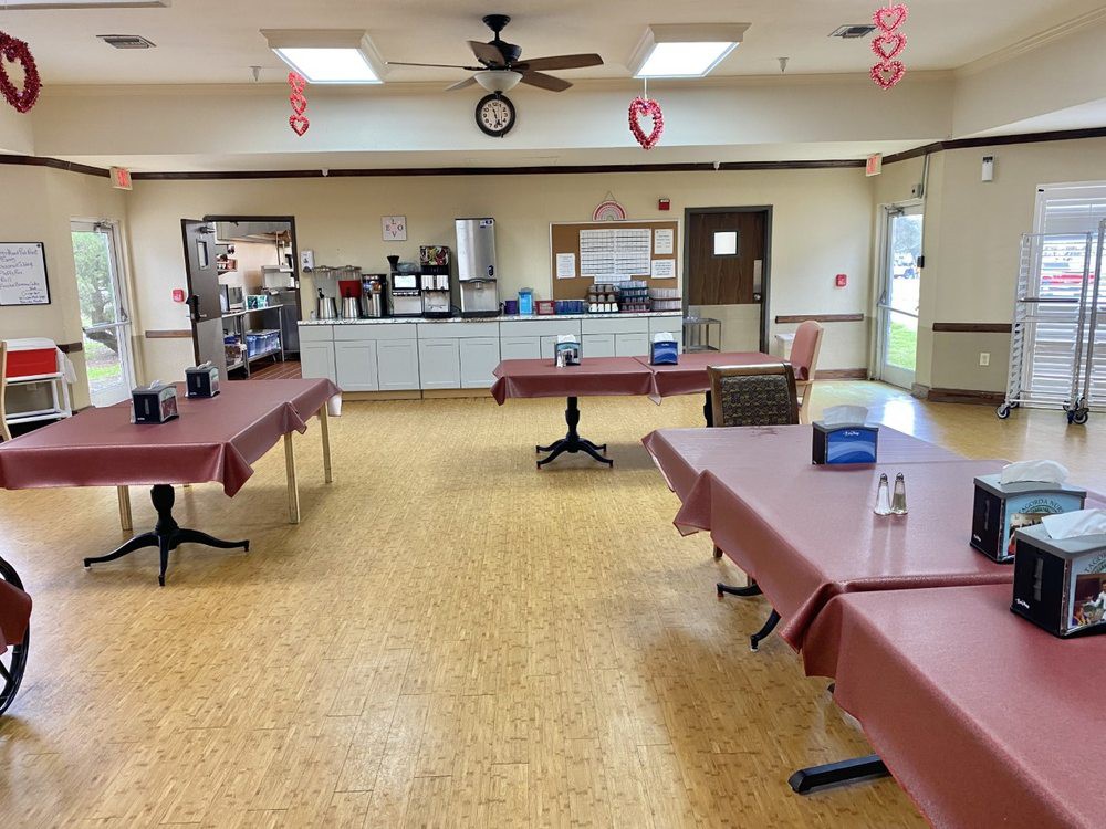 An empty community center room with decorated tables and a kitchen area in the background.
