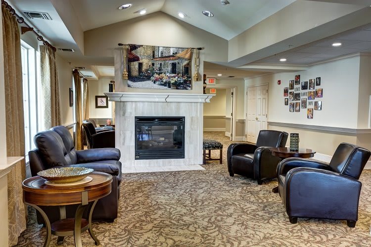 A cozy living room with armchairs and a fireplace, featuring warm lighting and carpeted flooring.