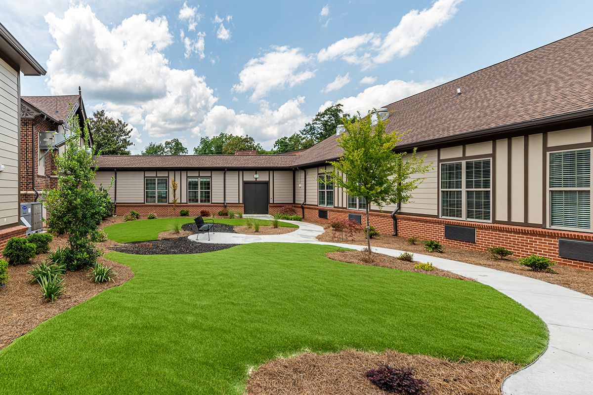 A pleasant view of a landscaped garden with a modern building in the background, featuring a well-maintained lawn and clear skies.