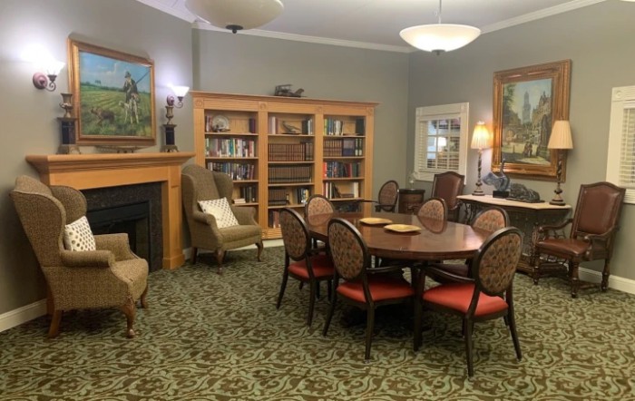 A cozy library room with bookshelves, a fireplace, and a large table surrounded by chairs.