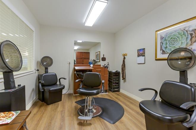 An empty barbershop with chairs and a mirror, featuring a wooden floor and bright lighting.