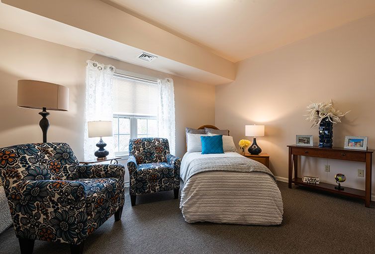A cozy bedroom with a single bed, two patterned chairs, and warm lighting.