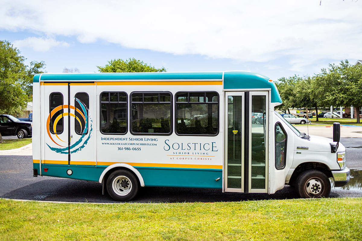 A white and teal shuttle bus with Solstice branding parked on green grass under a clear sky.