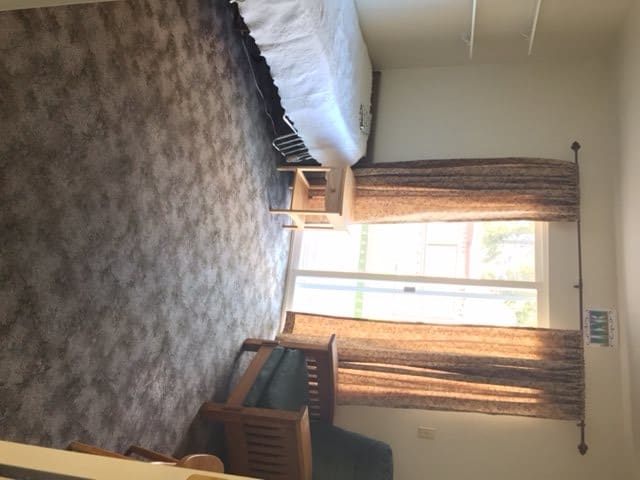 A cozy bedroom with a bed, carpeted floor, and large window allowing natural light.