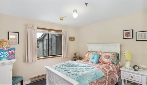 A cozy bedroom with a neatly made bed, colorful bedding, and a large window offering natural light.