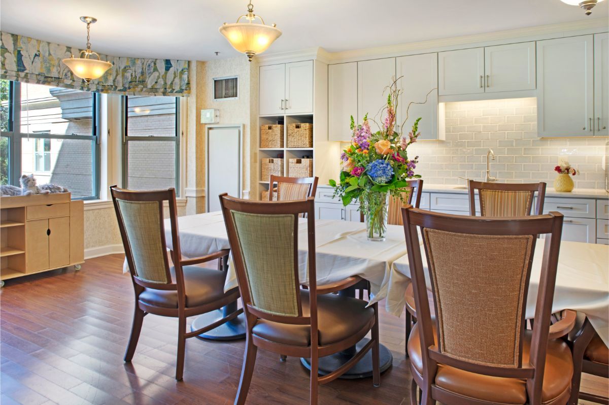 A modern dining area with a table and chairs, featuring a vase of flowers and ample natural light.