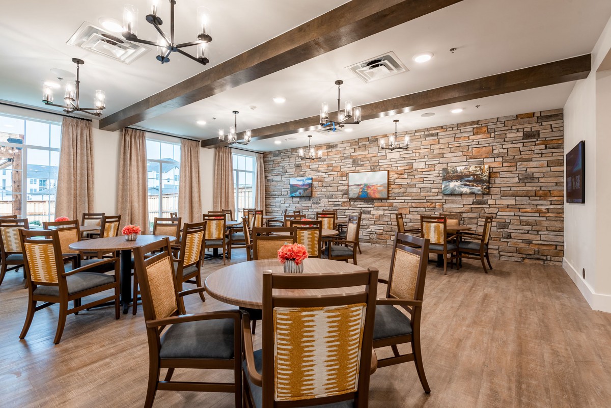 A cozy dining room with wooden furniture and chandeliers, featuring a stone accent wall.