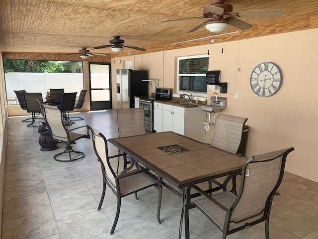 A spacious outdoor patio featuring a dining table, kitchenette, and ceiling fans.