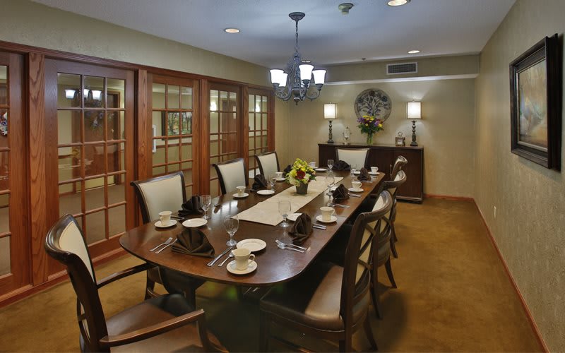 An elegantly set dining room with a large wooden table and comfortable chairs, featuring sophisticated decor and soft lighting.