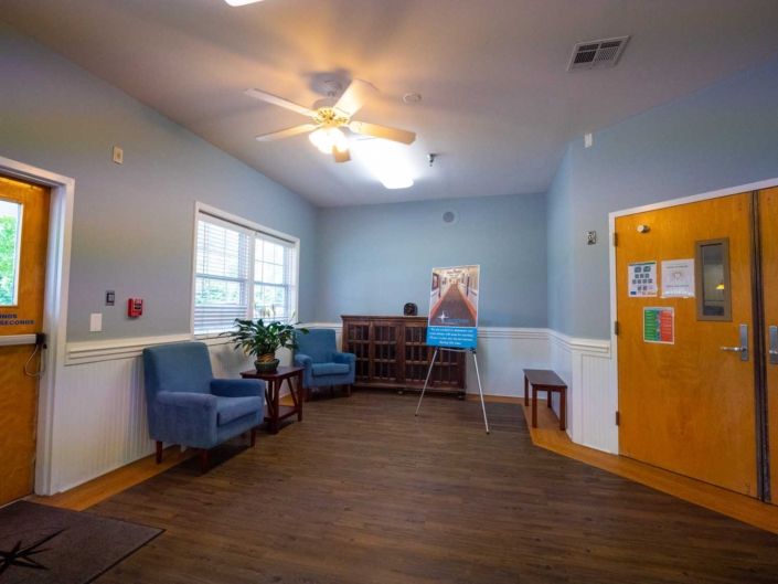 A cozy living room with blue chairs, a bookshelf, and artwork on the wall.