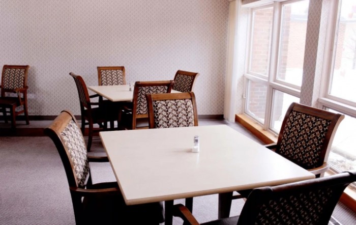 A quiet dining area with several tables and chairs, illuminated by natural light from a large window.