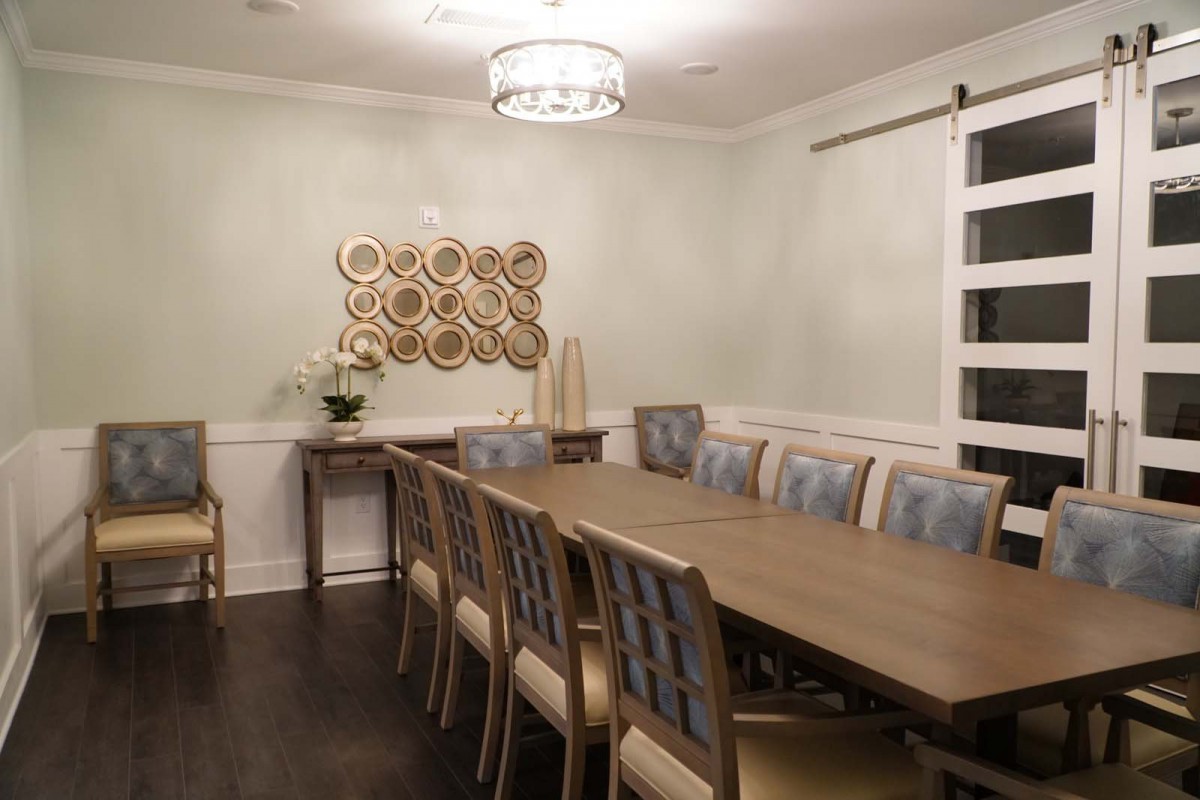 A modern dining room featuring a long table with multiple chairs, a chandelier above, and wall art for decoration.