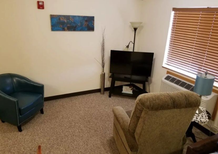 A cozy living room with a television, armchair, and window blinds.