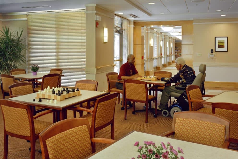 A quiet room in a retirement home with elderly residents engaging in activities such as playing chess.