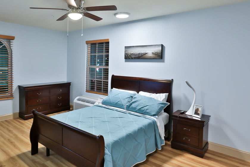 A cozy bedroom featuring a bed with blue bedding, wooden furniture, and a ceiling fan.