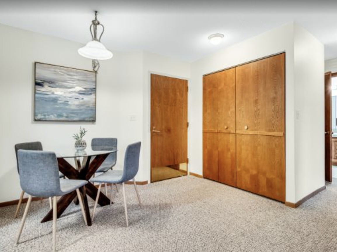 A modern dining area featuring a round table with four chairs, a large painting on the wall, and wooden closet doors.