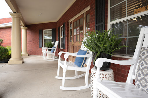 A cozy porch featuring white rocking chairs and lush plants, perfect for relaxation.