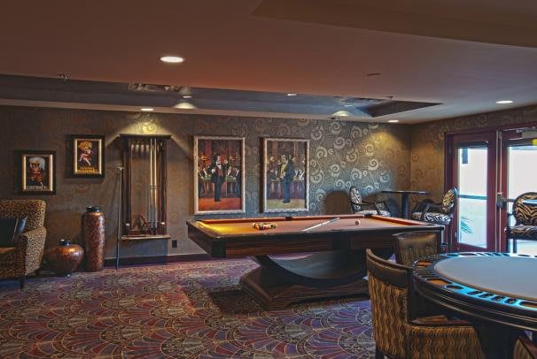 A luxurious billiard room featuring a stylish pool table, artwork-adorned walls, and cozy seating.